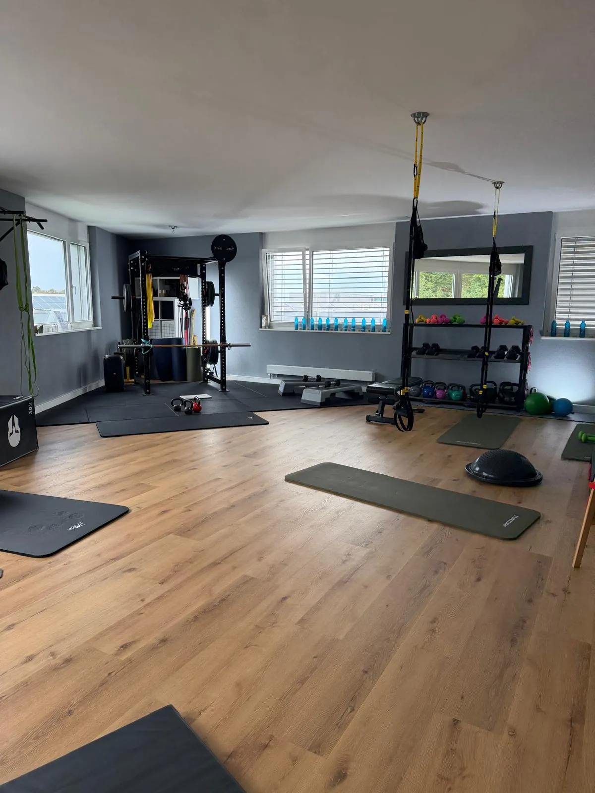 Salle de coaching lumineuse : parquet, rack, kettlebells et sangles TRX